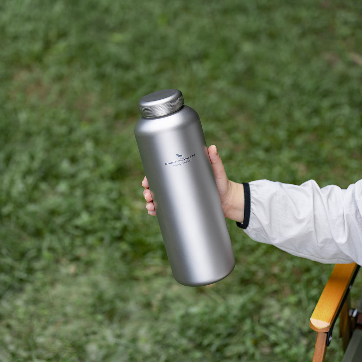Hand holding sandblasted titanium water bottle with titanium screw cap outdoors