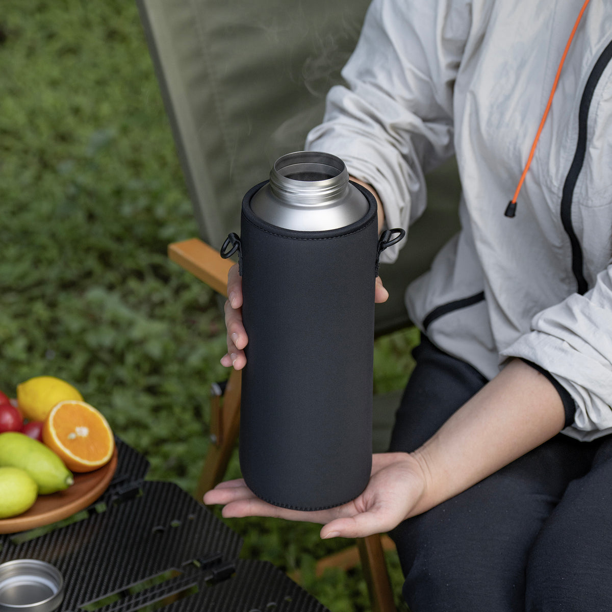 Holding titanium water bottle in insulated black sleeve with steaming hot drink
