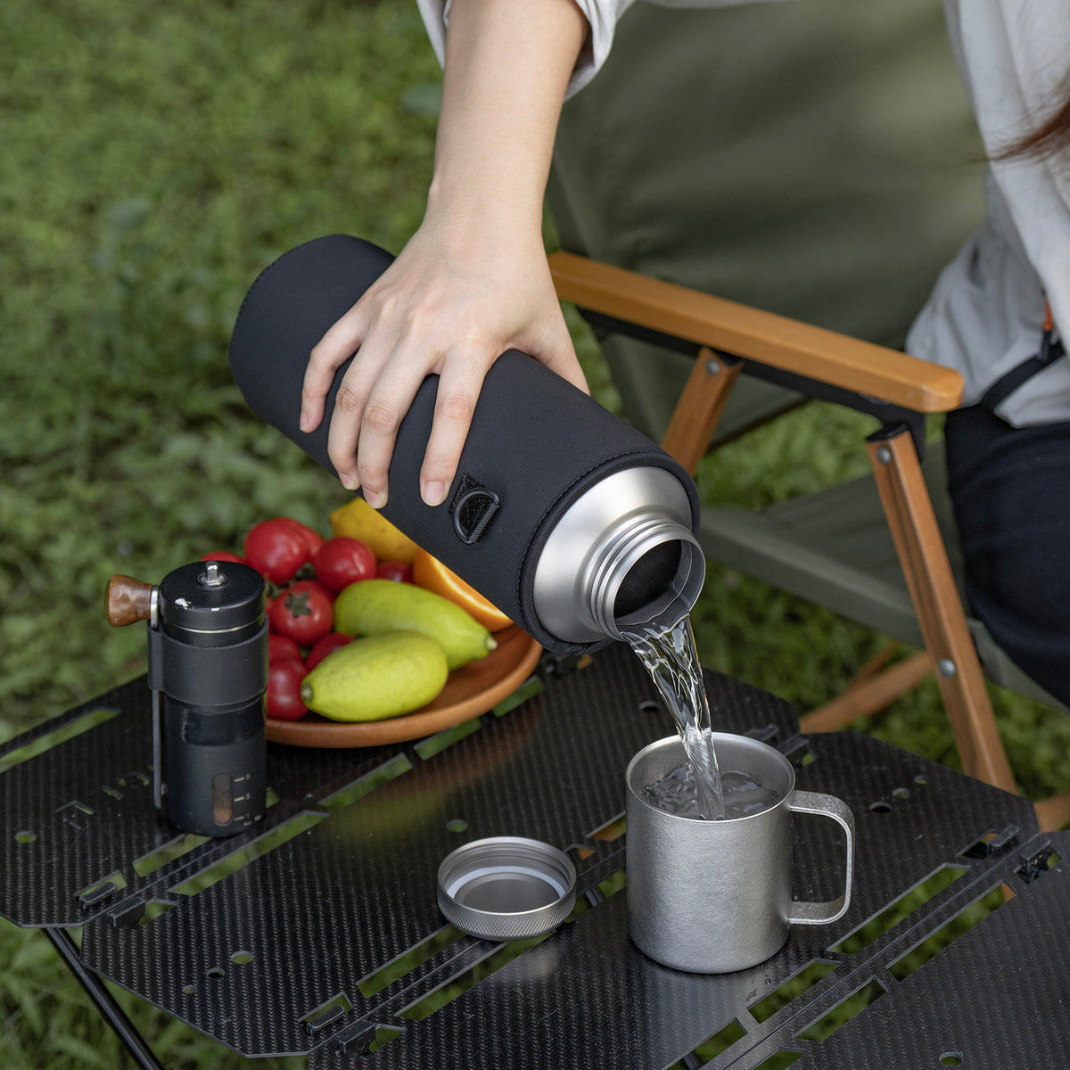 Pouring hot water from insulated titanium bottle into camp mug at campsite table