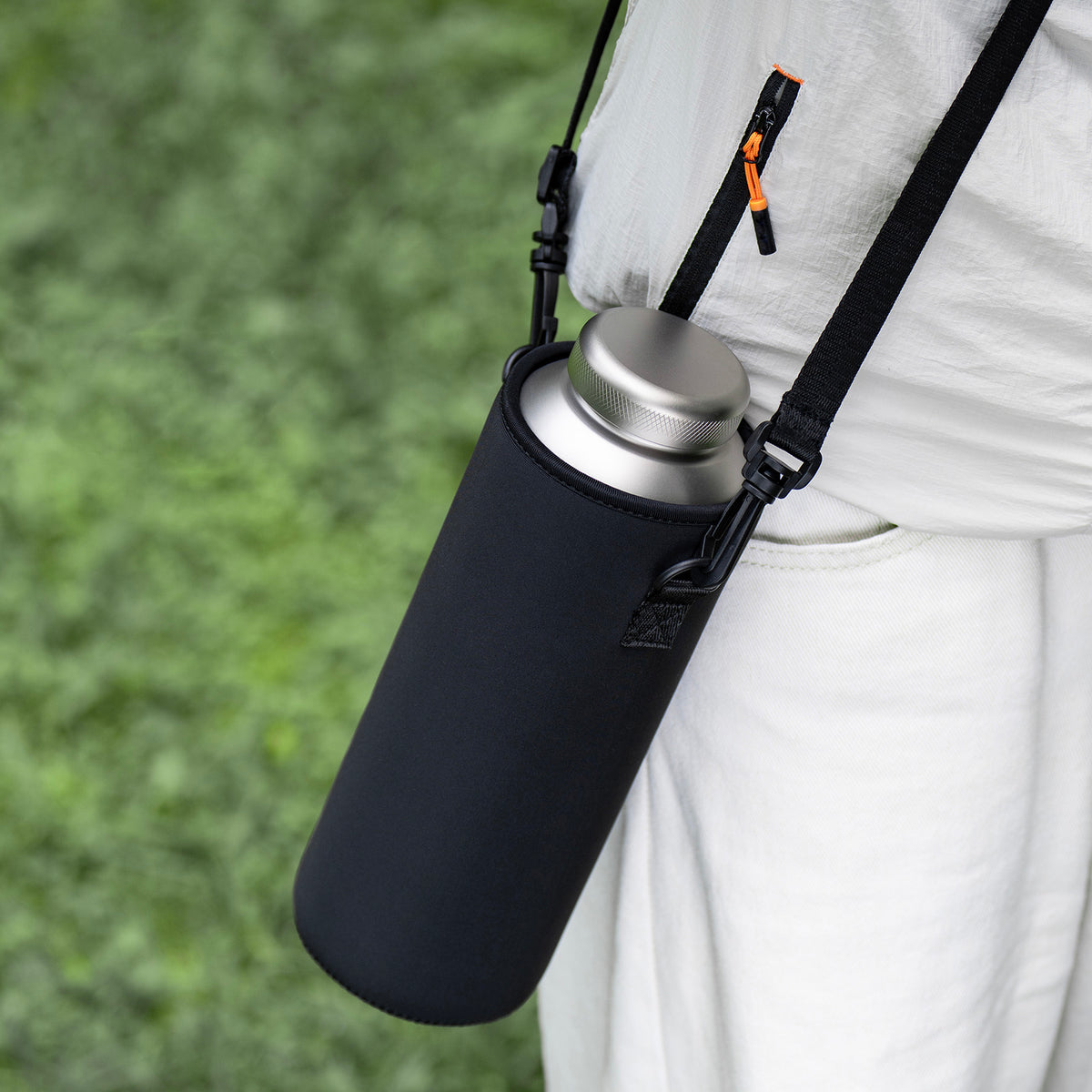 Holding titanium water bottle in insulated black sleeve with steaming hot drink