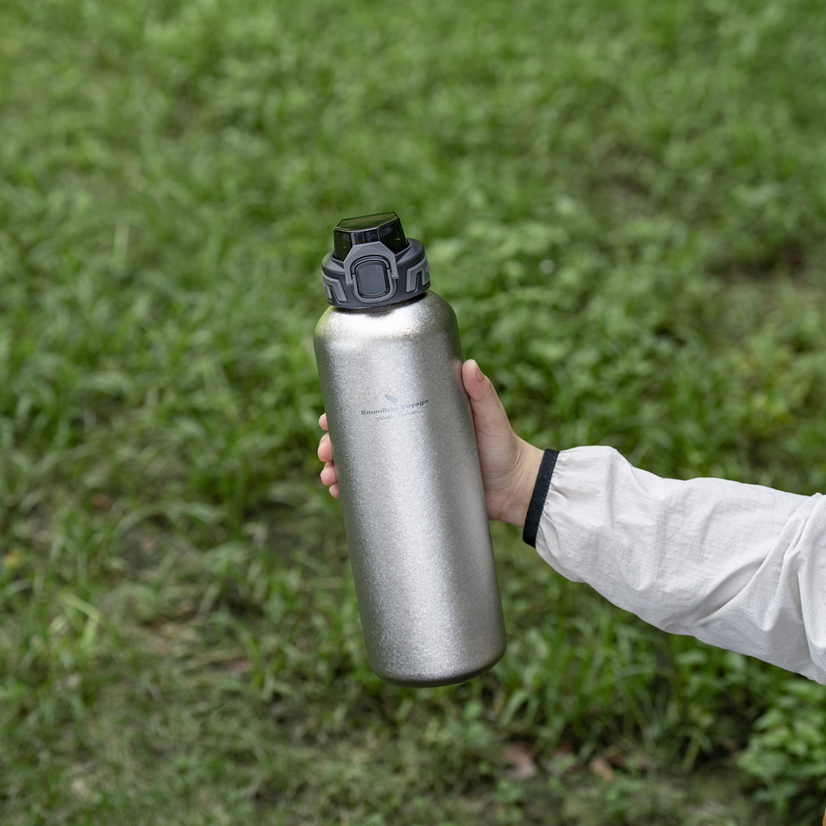 Hand holding crystallized silver 1500ml titanium bottle with PP flip lid outdoors