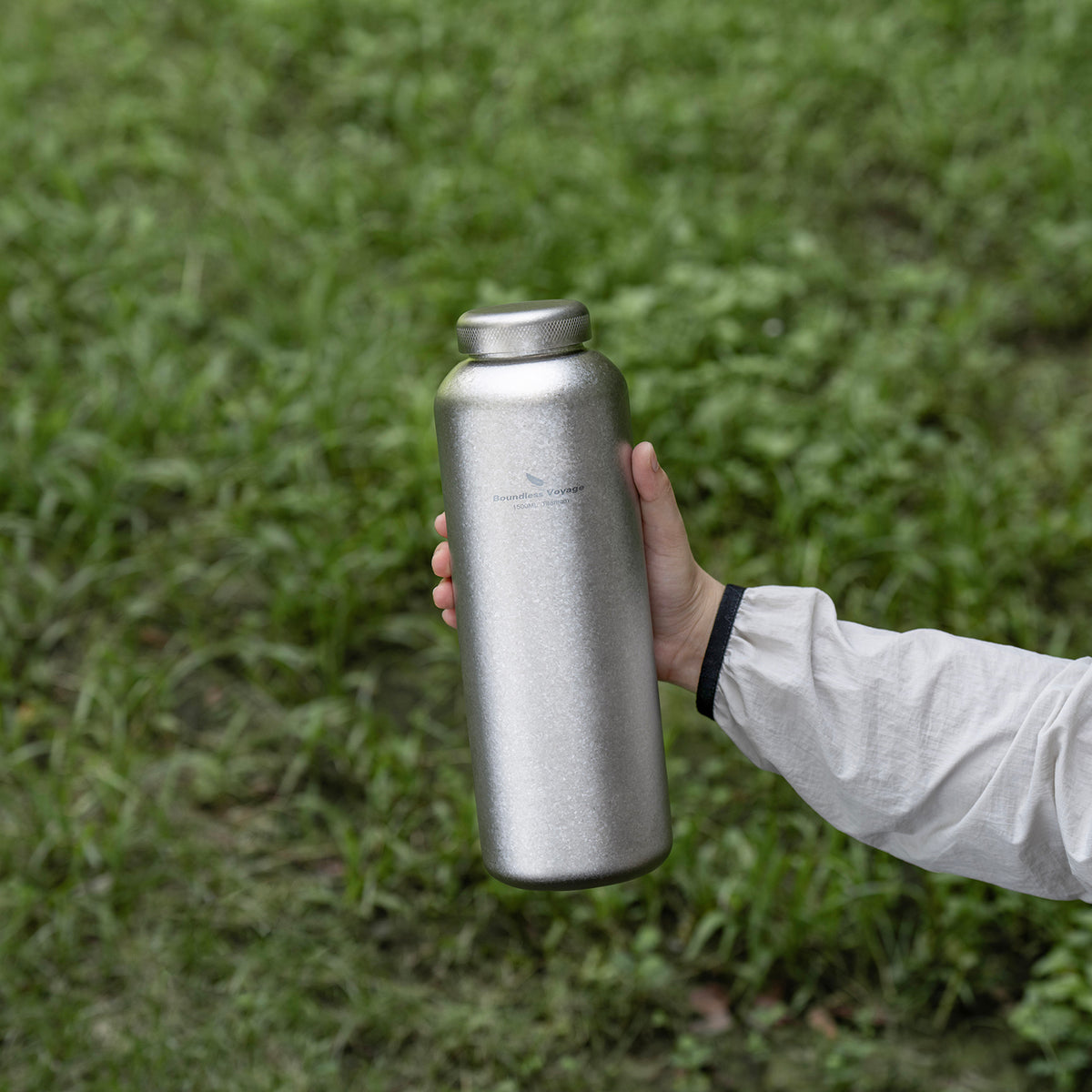 Hand holding crystallized silver titanium bottle with titanium screw cap outdoors