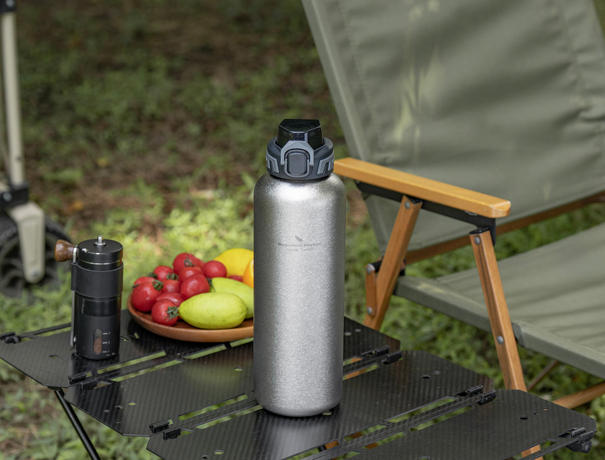 Crystallized silver titanium water bottle with PP flip lid standing on outdoor camp table