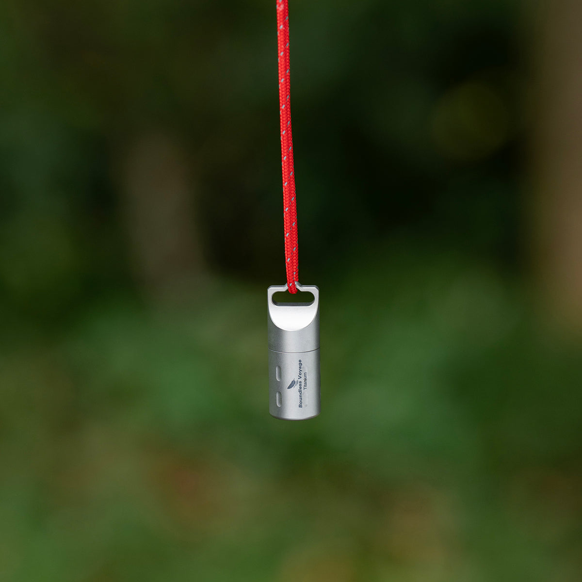 Ti9009A titanium pill container hanging on red lanyard outdoors for easy carry