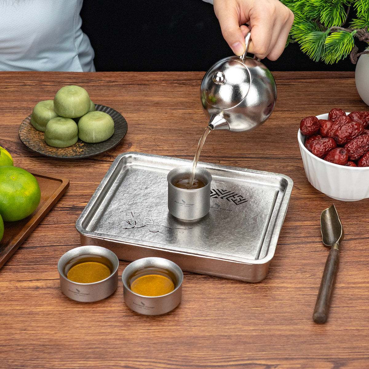 Pouring freshly brewed tea from titanium teapot into double-wall cup on the tea tray